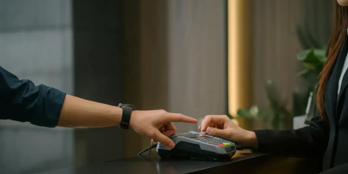 A guest taps their smartwatch to pay at a sleek hotel check-in counter
