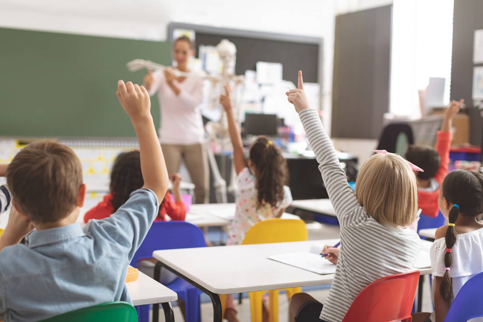 Rear,View,Of,Kids,Raising,Hands,While,Teacher,Explaining,The hotels give back in schools